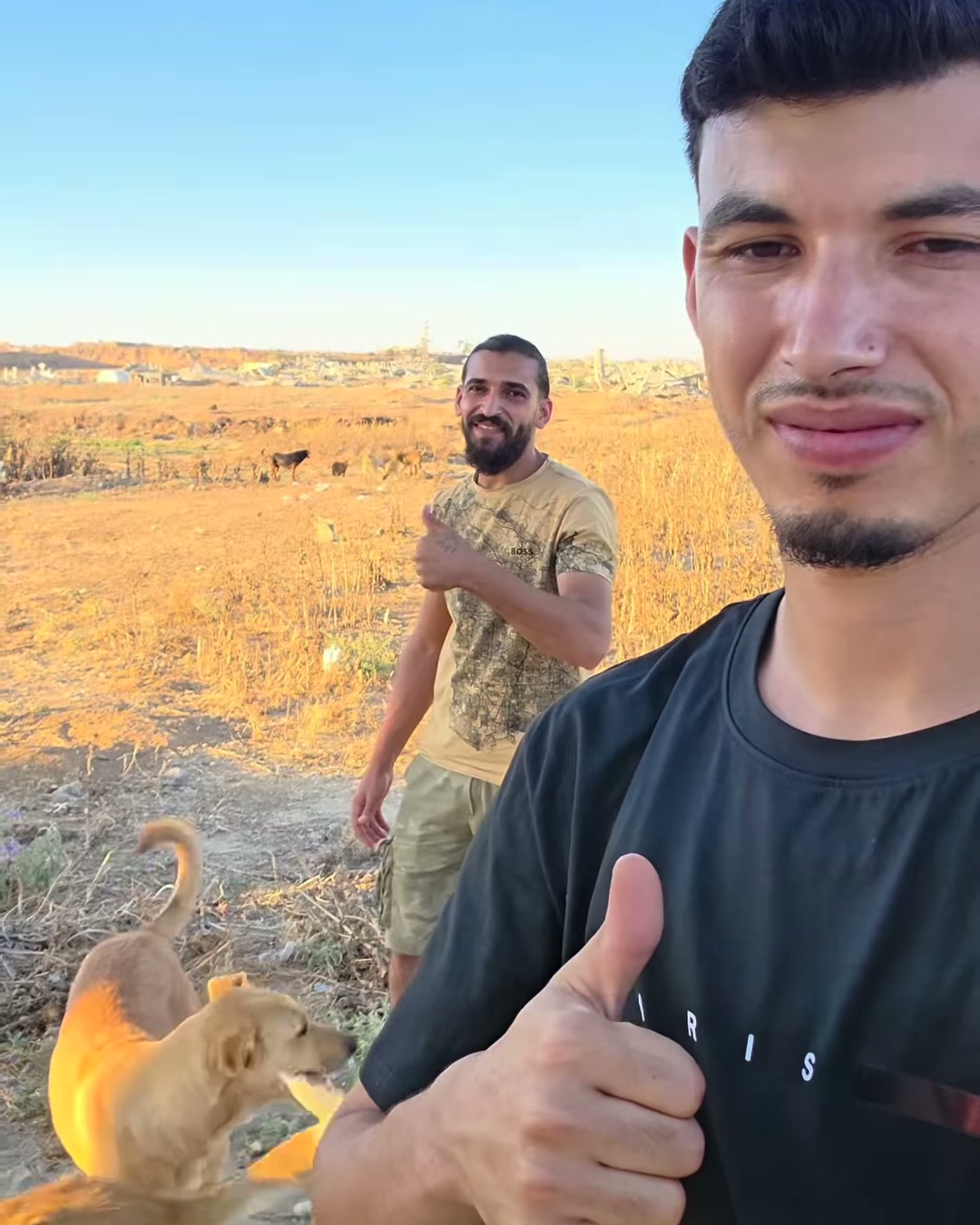 The two young men of the Gaza Animal Rescue Team outdoors in Gaza, one giving a thumbs-up, with a dog beside them